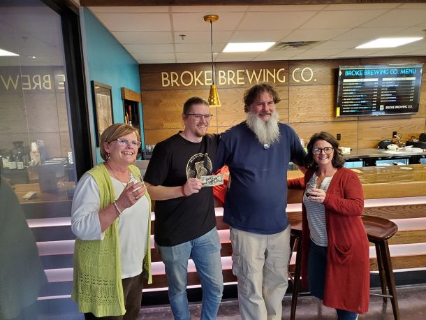 broke brewing co history photo of owners holding the first dollar and members of nwokc chamber of commerce all standing in tap room